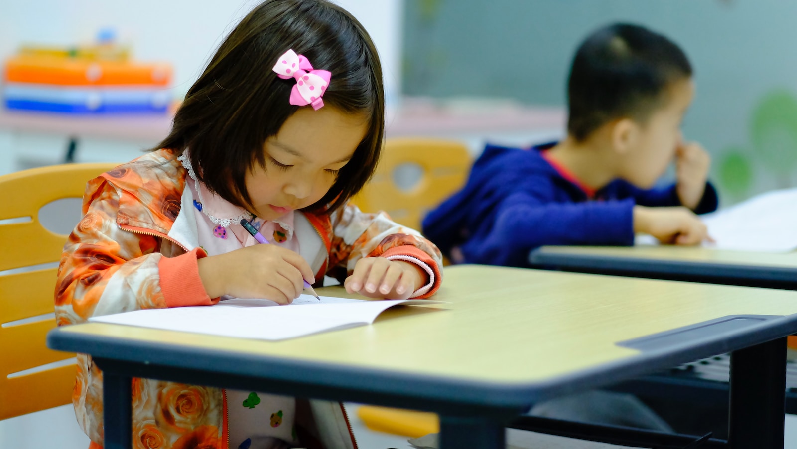 a little girl sitting at a table writing on a piece of paper