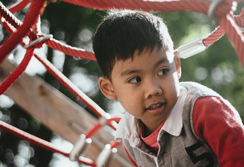 boy in gray and red hoodie standing on red metal fence during daytime