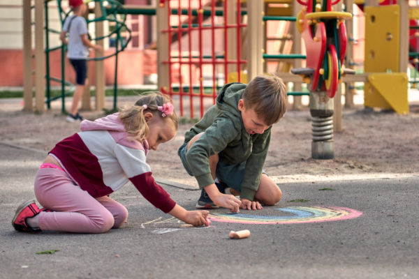 Kids Paint Outdoors. Boy Drawing A Rainbow Colored Chalk On The Asphalt The Playground