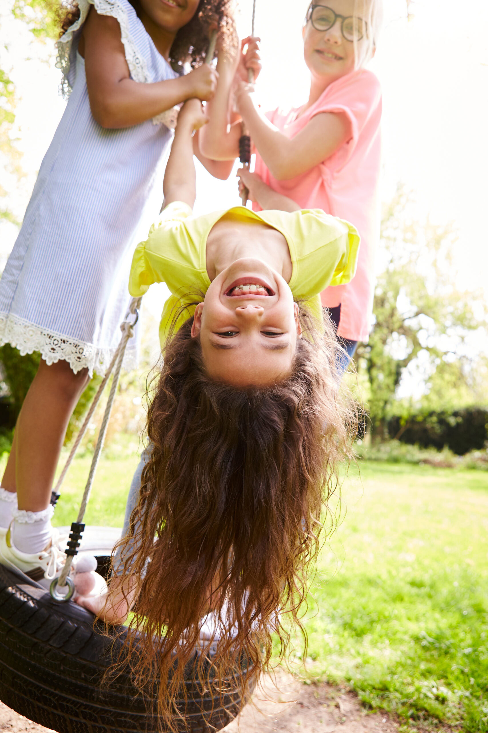 Group Of Girls Having Fun With Friends Playing On Tire Swing In Garden