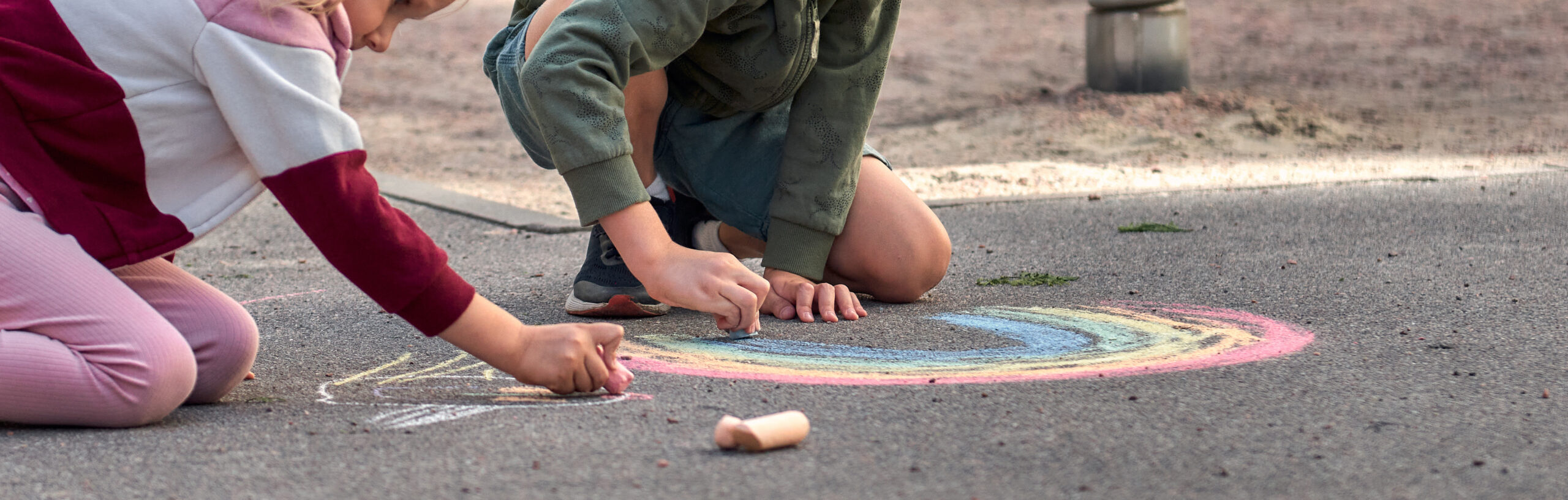 Kids paint outdoors. boy drawing a rainbow colored chalk on the asphalt the playground