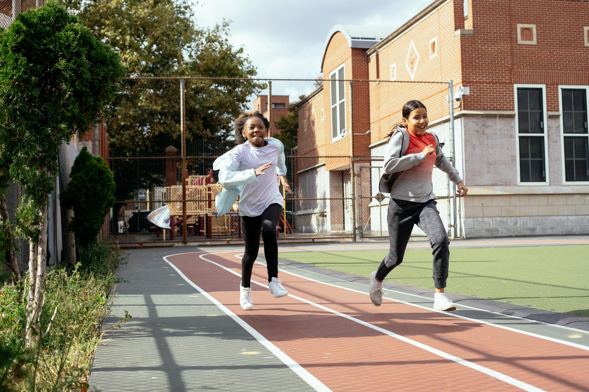 Full length of multiracial girls in sportswear and sneakers racing with each other on sports ground near school