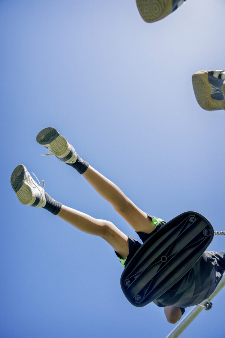 Boy swinging on a playground. Close up. Blue sky.