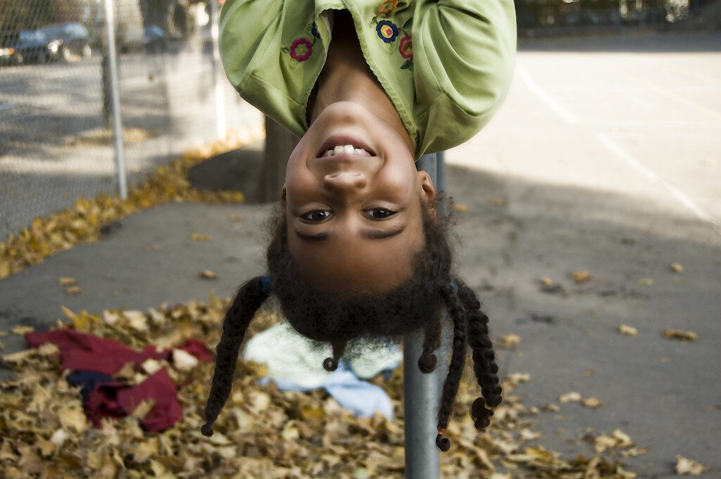 Young girl with pig tails hanging upside down on a playground